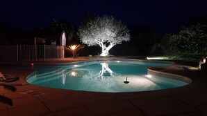 A swimming pool at night with a tree in the center, surrounded by a fence and illuminated by lights. - Maison Pleine de Charme (Saint-Féliu-d'Avall)