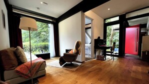 Un salon moderne avec un canapé, un fauteuil et un piano, de grandes fenêtres et une porte rouge.