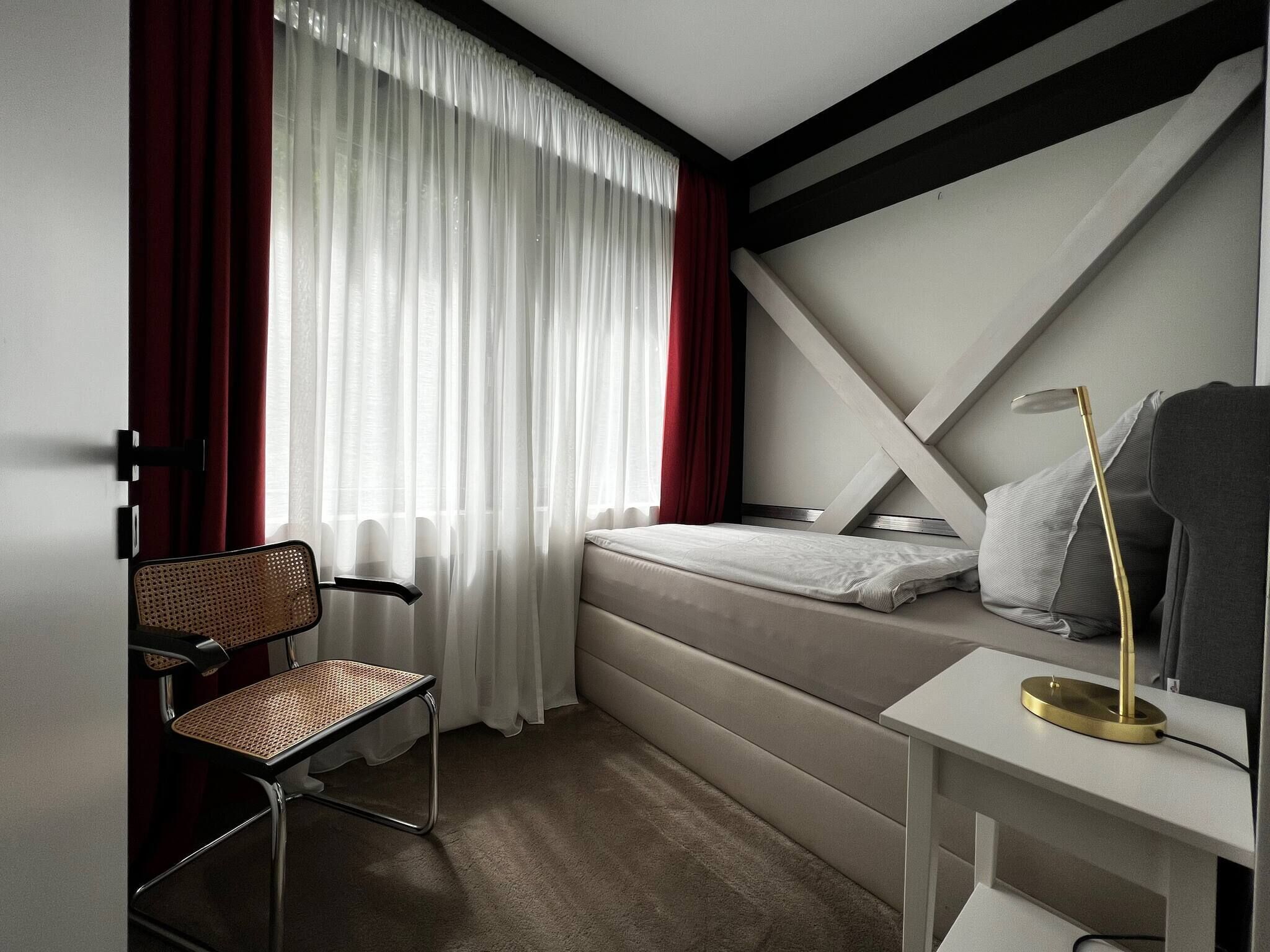 Ein kleines Hotelzimmer mit Bett, Stuhl, Nachttisch und Schreibtisch.