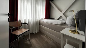 Une chambre d’hôtel de taille réduite, comprenant un lit, une chaise, une table de chevet et un bureau.