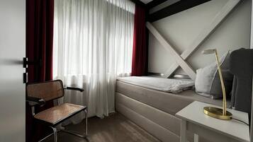 Ein kleines Hotelzimmer mit Bett, Stuhl, Nachttisch und Schreibtisch.