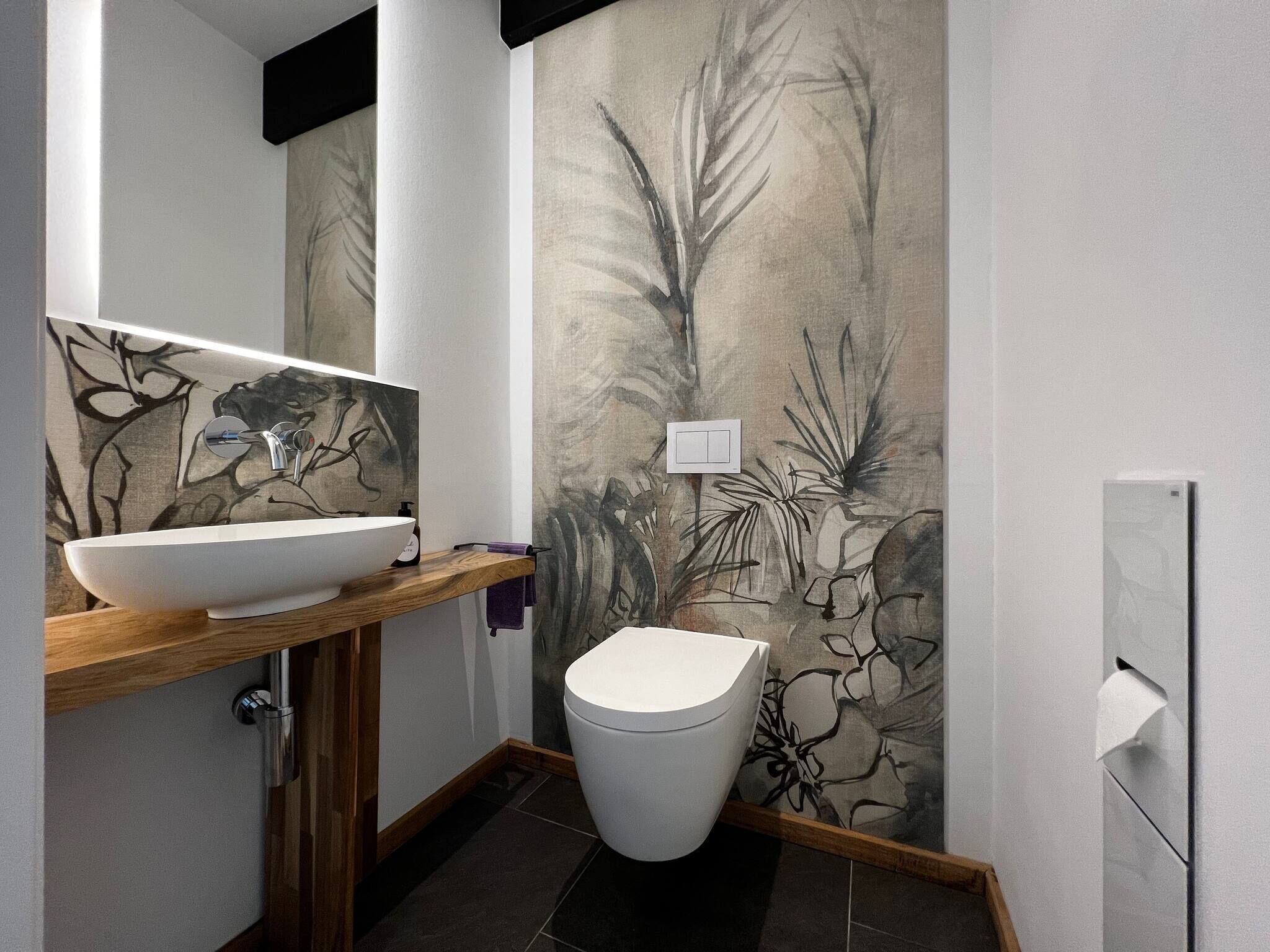 Ein modernes Badezimmer mit einem weißen Waschbecken, einer Toilette und einer Wand mit einem botanischen Wandbild.