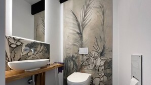 Une salle de bain moderne avec un lavabo blanc, des toilettes et un mur orné d’une fresque à motifs végétaux.