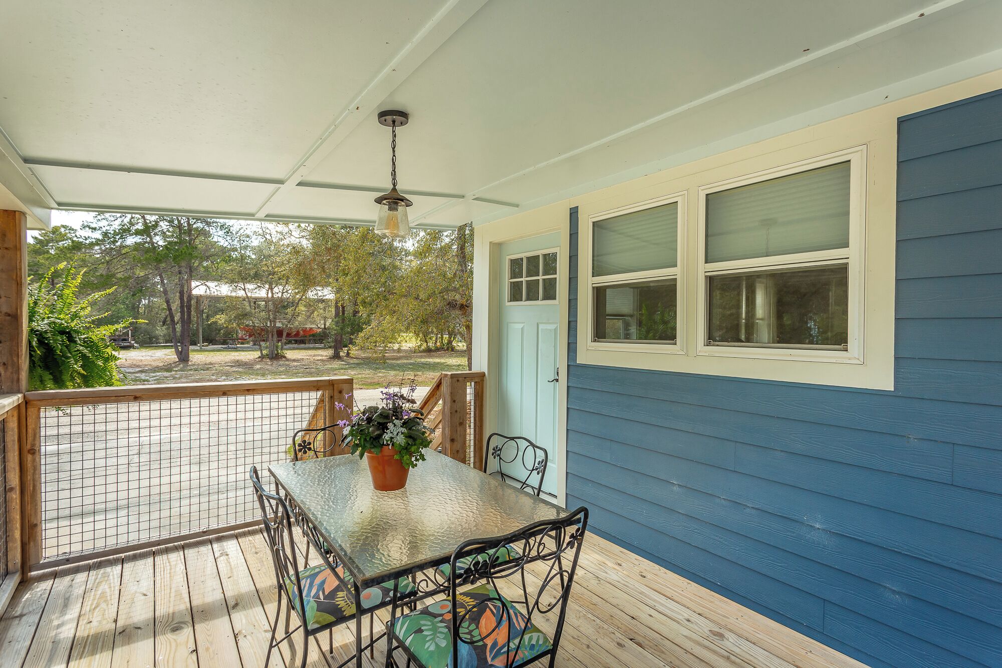 A covered porch with a table and chairs, a potted plant, and a view of the outdoors.