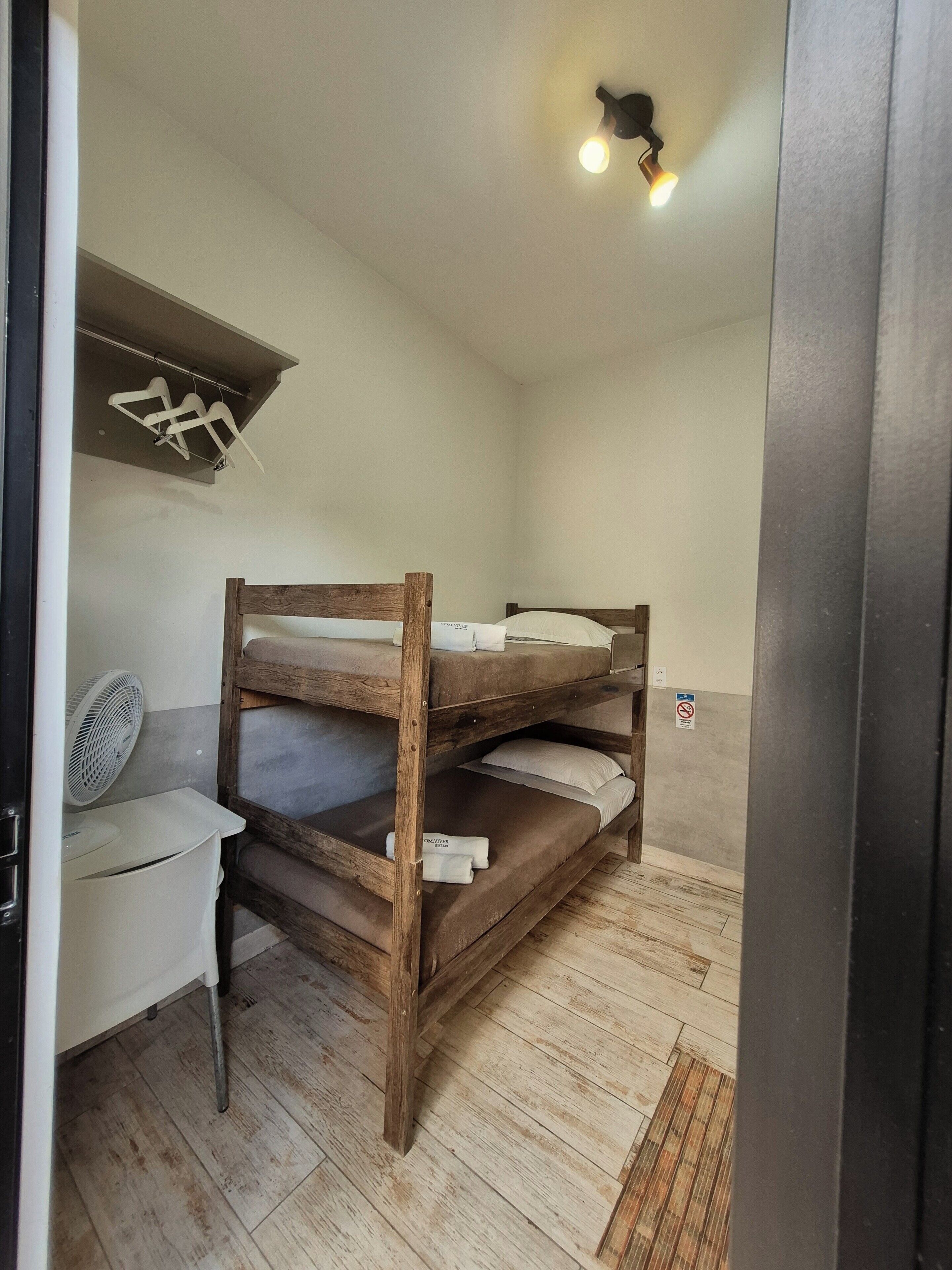 Een stapelbed met houten frame, een klein bureau met stoel, en een wandlamp.