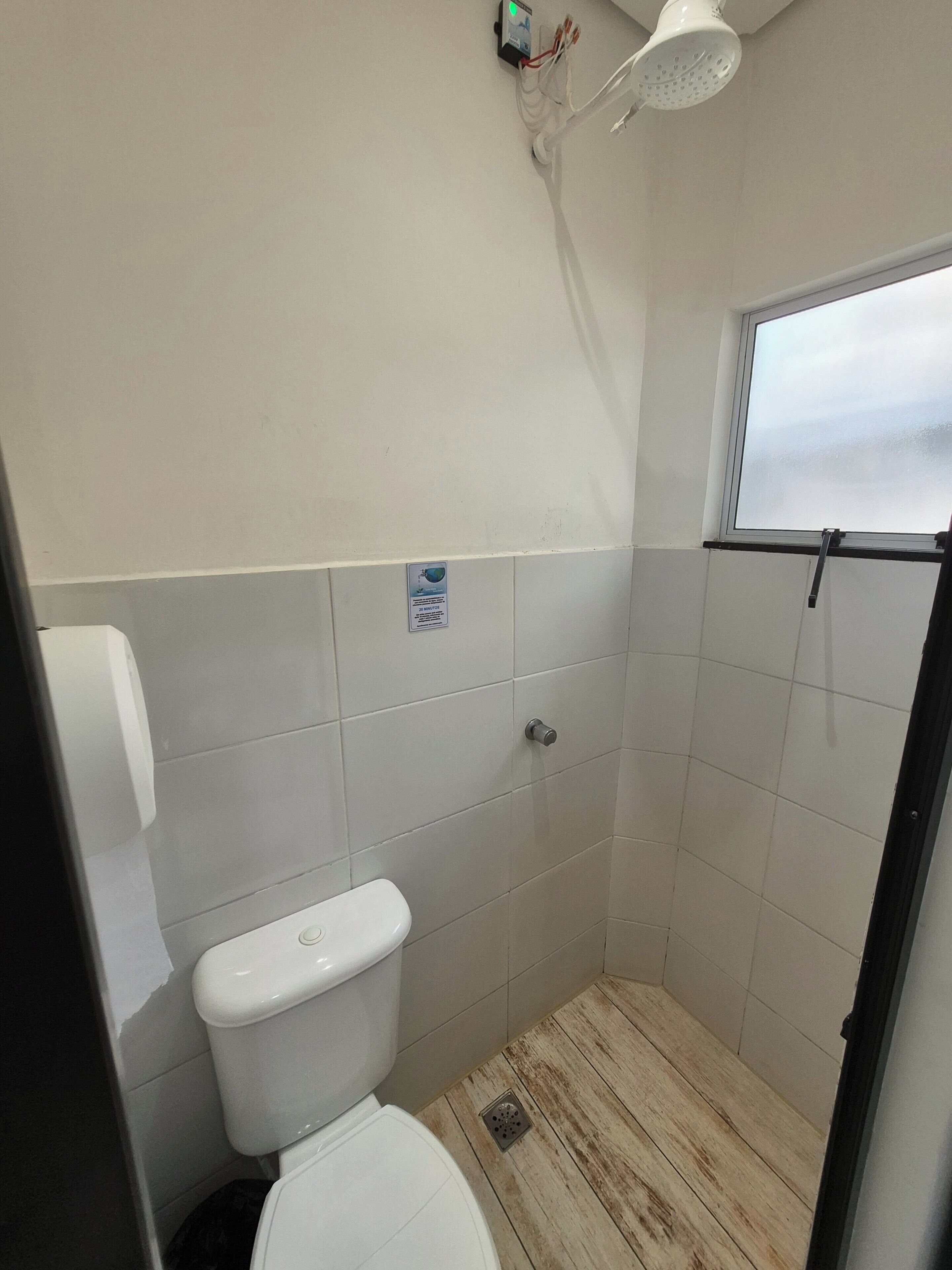 Ein kleines, abgeschlossenes Badezimmer mit Toilette, Duschkopf und Fenster.