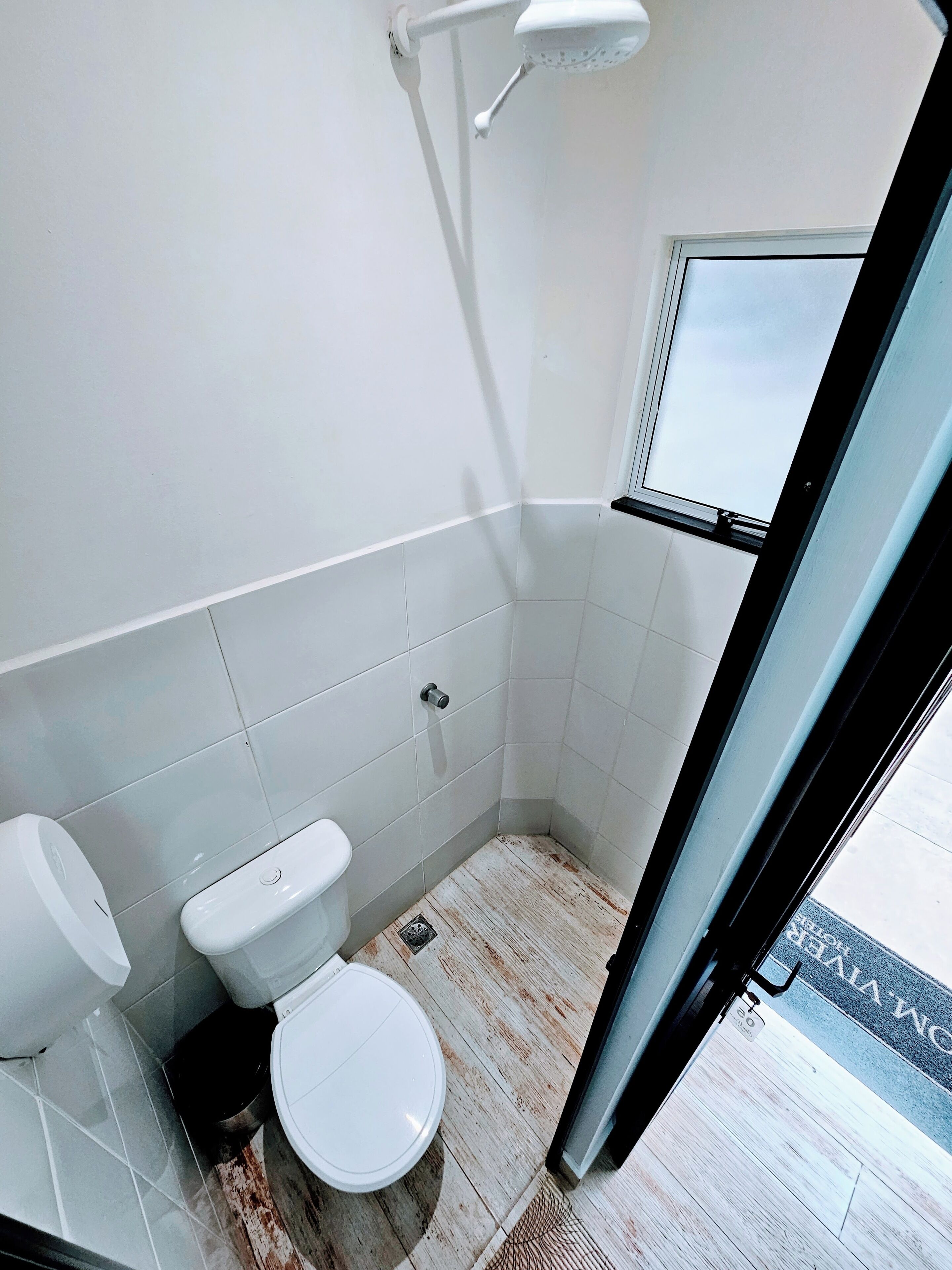 A small, modern bathroom with white fixtures, a shower, and a window.