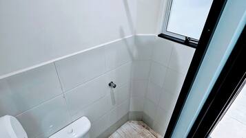 A small, modern bathroom with white fixtures, a shower, and a window.