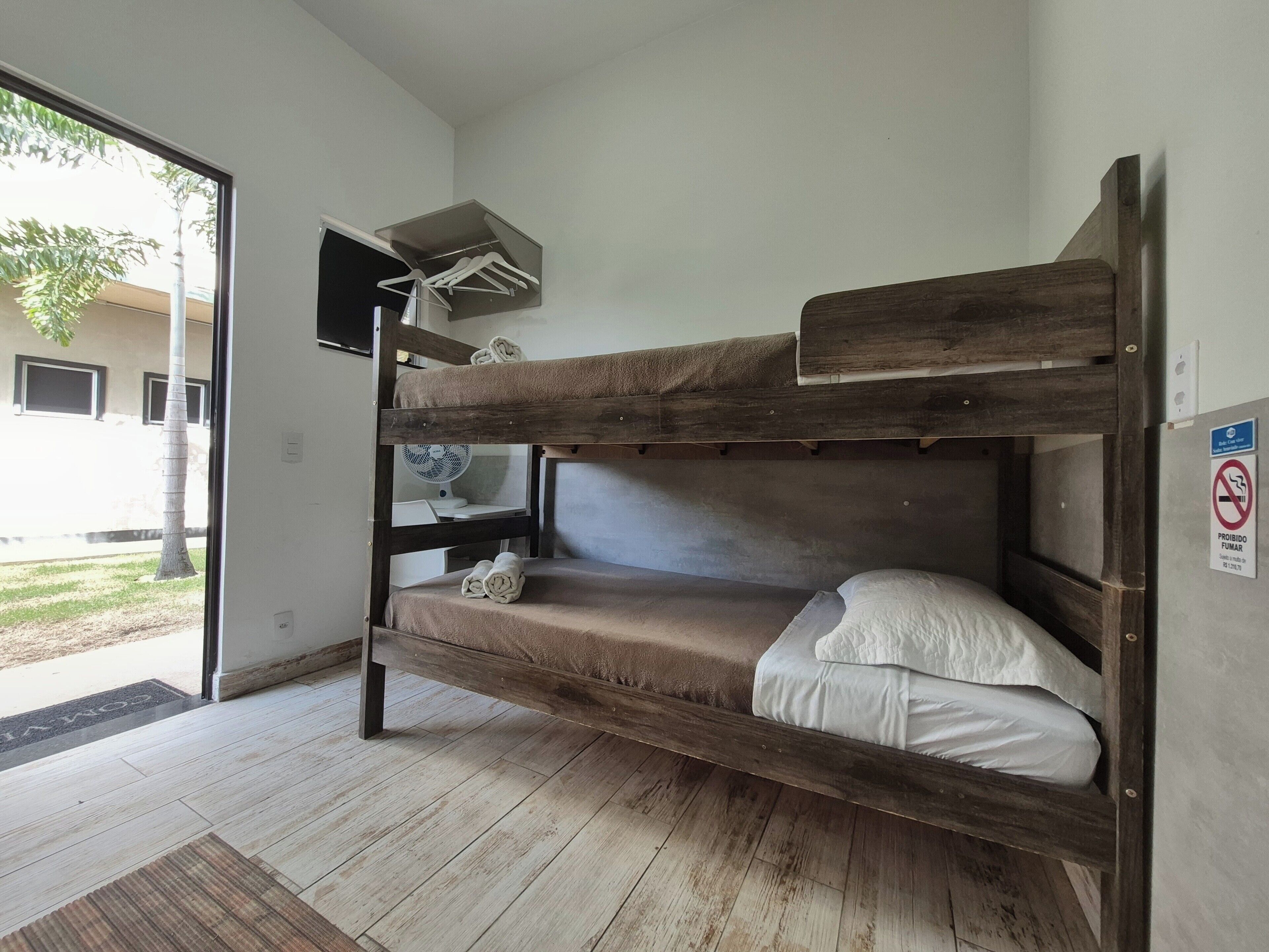Ein Stockbett mit Holzbalken, eine kleine Ablage darüber und ein weißes Kopfkissen im unteren Bett.