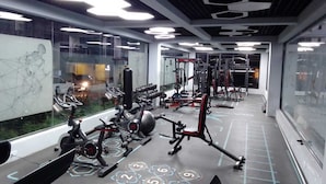 Ein Fitnessstudio mit unterschiedlichen Trainingsgeräten, darunter Laufbänder, Gewichte und ein Rudergerät.