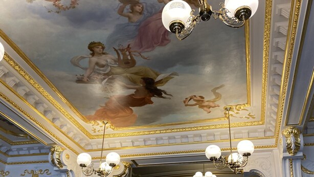 A grand staircase with ornate railings and a ceiling mural depicting cherubs.