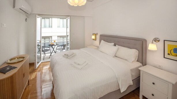 Ein modernes Hotelzimmer mit einem großen Bett, Nachttischen, einem kleinen Schreibtisch und einem Balkon mit Sitzgelegenheiten.