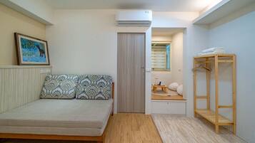Una camera da letto con un letto, un armadio in legno, una piccola area salotto con una finestra e un condizionatore.