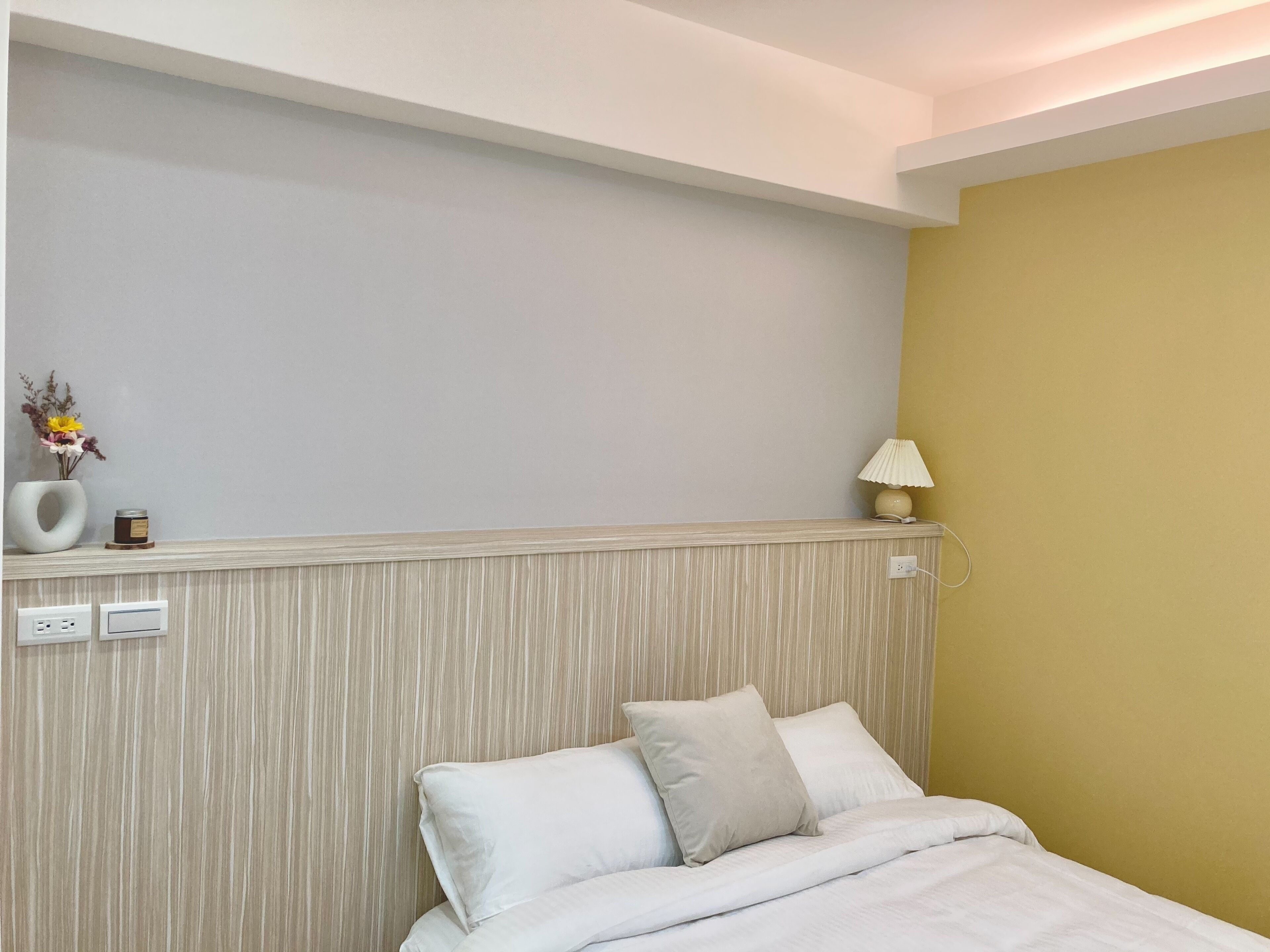 Habitación de hotel con una cama, una mesita de noche con lámpara y un enchufe en la pared.
