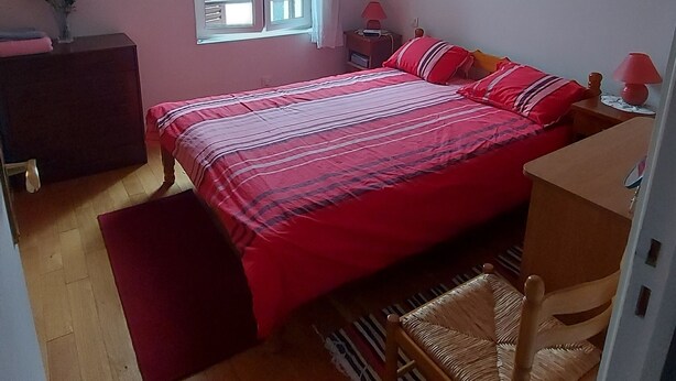 Une chambre à coucher comprenant un lit, une chaise, un bureau, une commode, une fenêtre avec des rideaux et un luminaire suspendu.