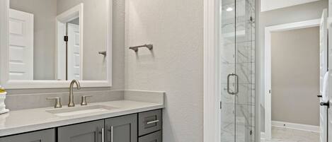 Un baño con lavamanos doble, un espejo grande y cabina de ducha de cristal.