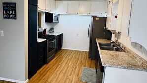 A modern kitchen with white cabinets, a microwave, a stove, and a refrigerator. There is a welcome sign on the wall and a rug on the floor.