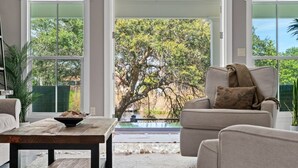 Ein Wohnzimmer mit einer Couch, einem Couchtisch und Blick auf Bäume und ein Wasserspiel.