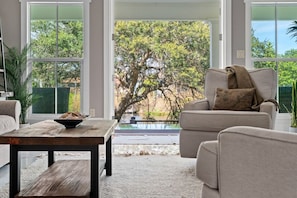 Una sala de estar con sofá, mesa de centro y vistas a árboles y una fuente de agua.
