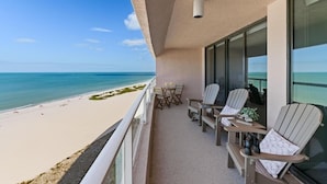 A balcony with a view of the beach, furnished with chairs and a table.