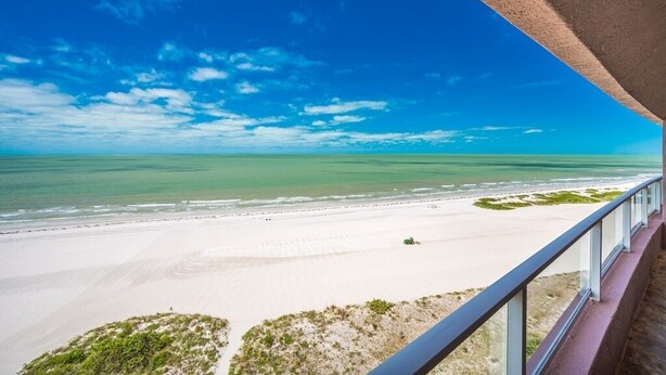A beach view from a balcony with a clear sky and calm sea.