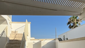 A covered outdoor area with a staircase leading to a door, a palm tree, and a clear blue sky. - The lily vacation home  (Marina di Mancaversa)