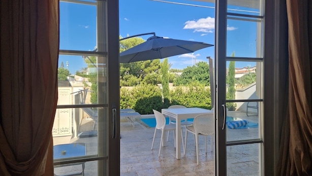 An open glass door leading to an outdoor patio with a pool, white chairs, and a table. - The lily vacation home  (Marina di Mancaversa)
