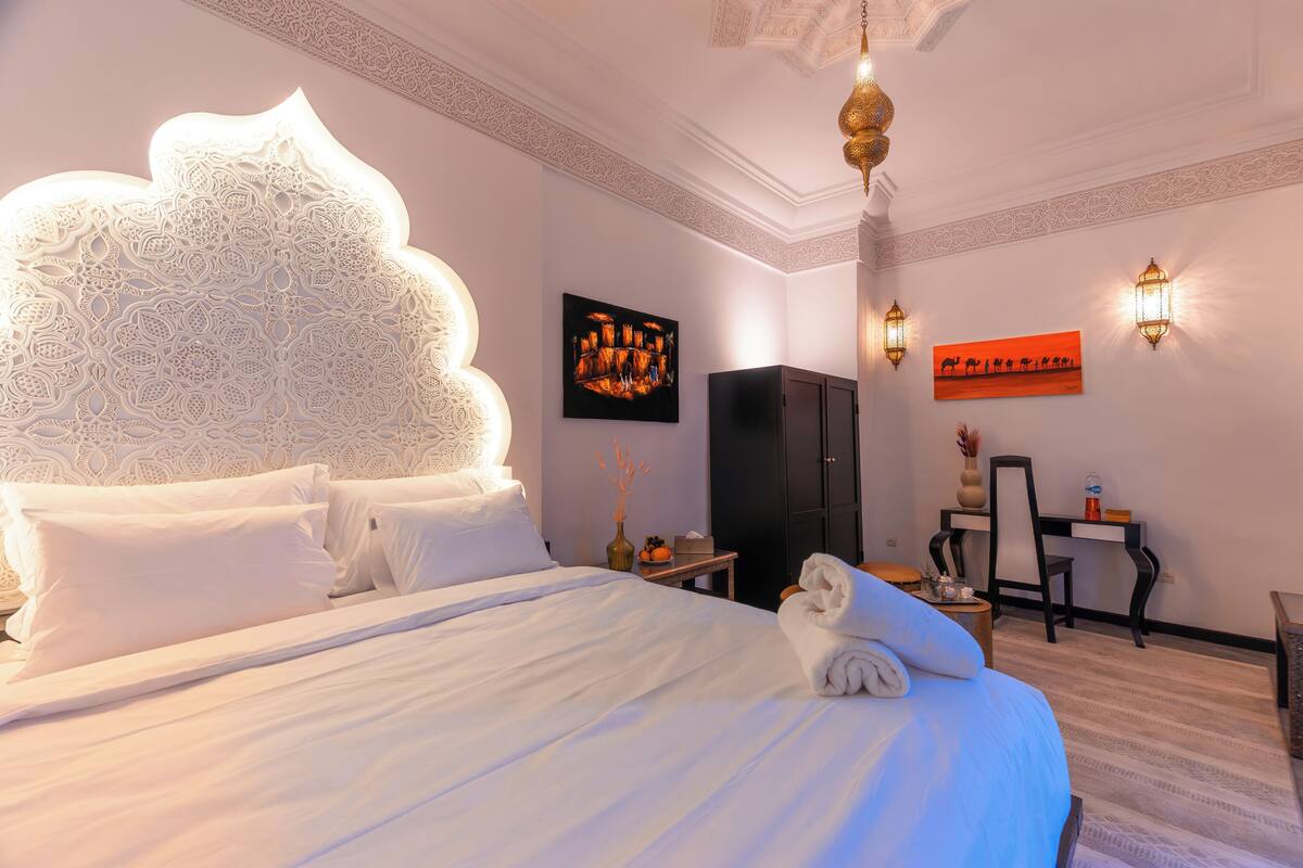 A hotel room with a large bed, a desk, and a wardrobe.