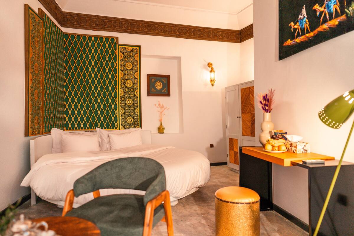 A hotel room with a bed, a desk, a chair, a lamp, and a decorative wall panel.