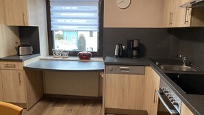 Et kompakt køkken med indbygget opvaskemaskine, kaffemaskine og brødrister.