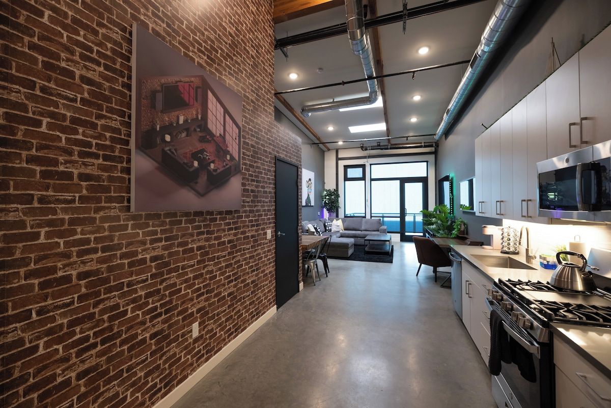 A modern kitchen with stainless steel appliances, a brick wall, and a dining area with a sofa and table.