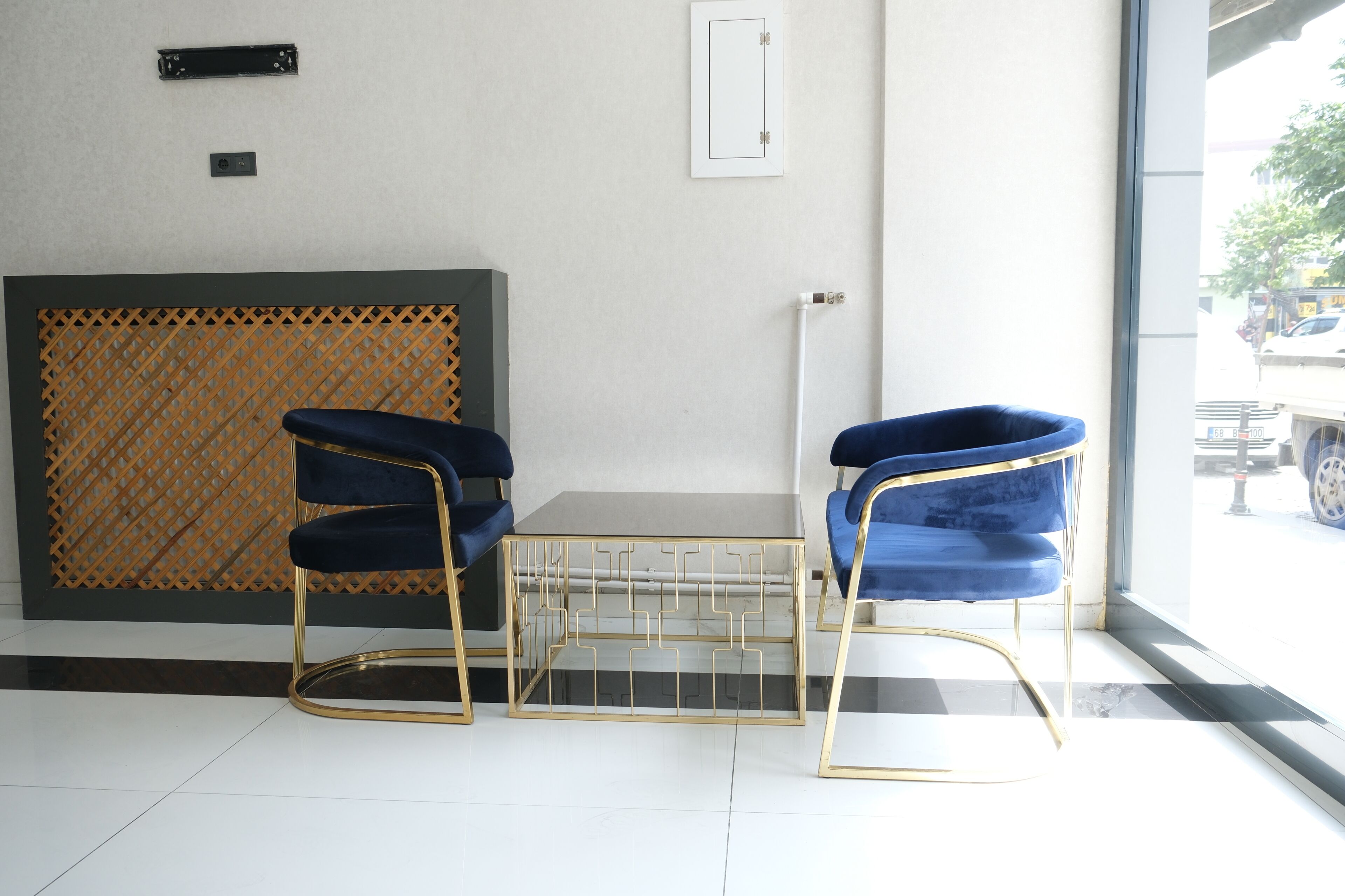 Una habitación con dos sillas azules, una mesita, un panel de celosía de madera y vistas al exterior a través de un gran ventanal.