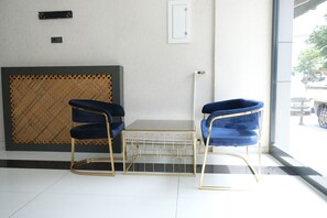 A room with two blue chairs, a small table, a wooden lattice partition, and a view of the outside through a large window. - PLUSCITY HOTEL (Konya)