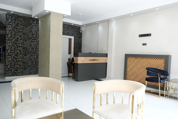 A reception area with a reception desk, two chairs, a patterned wall, and a patterned wall behind the desk. - PLUSCITY HOTEL (Konya)