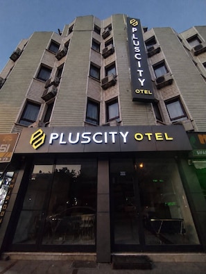 A PlusCity Hotel building facade with a prominent signage, large windows, and a modern architectural design.