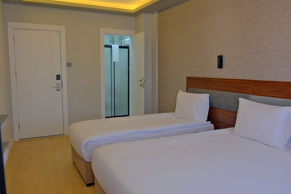 Une chambre d’hôtel avec deux lits, une tête de lit en bois, une porte blanche et une bouteille d’eau posée sur une étagère.