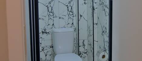A bathroom with a toilet, a shower enclosure, and marble-patterned walls.