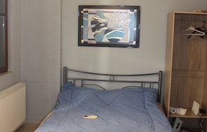 A bedroom with a bed, a framed picture on the wall, a radiator, and a wooden wardrobe with hangers. - Stunning one Bedroom Studio in Thessaloniki (Thessaloniki)