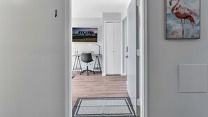 A hallway leading to a dining area with a 'WELCOME' sign, a painting of a flamingo, and a landscape photo on the wall. - Fenton Flats- Suite 1 With On Site Hot Tub and Personal Garage (Fenton Township)