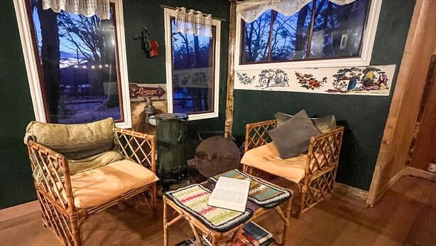 A cozy room with two wicker chairs, a small table with magazines, and a decorative wall with a forest scene.