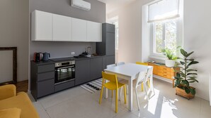 A modern kitchen with white cabinets, a built-in oven, and a dining area with a white table and yellow chairs. - Lake Design Guest House | Come Center (Como)