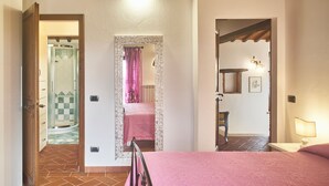 A bedroom with a bed, a nightstand, a lamp, and a door leading to a bathroom with a shower and a toilet.