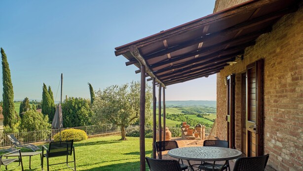 A patio with a table and chairs, a pergola, and a view of the countryside.