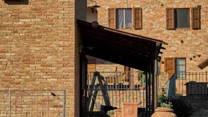 A traditional brick building with a wooden door, a covered outdoor seating area, and a large planter with flowers.