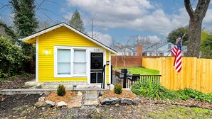 A yellow house with a black door, a small porch, and a wooden fence with an American flag. - Buttercup Cottage close to downtown Hendersonville fully fenced all pets welcome (Hendersonville)