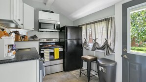 A compact kitchen with white cabinets, a black refrigerator, a microwave, an oven, and a trash bin. - Buttercup Cottage close to downtown Hendersonville fully fenced all pets welcome (Hendersonville)