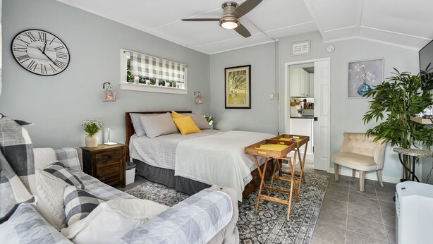 A bedroom with a bed, bedside tables, a clock, a ceiling fan, and a window with a view. - Buttercup Cottage close to downtown Hendersonville fully fenced all pets welcome (Hendersonville)