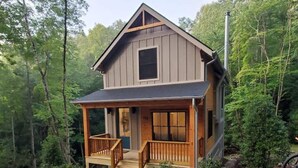 A cabin with a wooden porch and a small deck, surrounded by dense forest. - NEW mountain cottage between Dupont and Pisgah!! (Pisgah Forest)