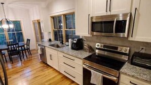 A modern kitchen with white cabinets, stainless steel appliances, and a wooden floor. - NEW mountain cottage between Dupont and Pisgah!! (Pisgah Forest)