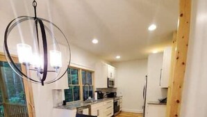 A modern kitchen with white cabinets, a wooden dining table, and a hanging light fixture. - NEW mountain cottage between Dupont and Pisgah!! (Pisgah Forest)